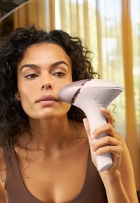 Dispositivo portatile per la rimozione dei peli con un corpo liscio e bianco e un accento rosa. Presenta un design ergonomico, una presa testurizzata e una grande testa di trattamento.