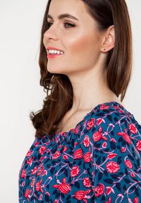 Blauwe bloemenblouse met rode en roze bloemenpatronen, geraffineerde halslijn en zachte stof. Glad textuur, korte mouwen en een ontspannen pasvorm.