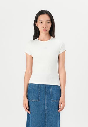 Haut court à manches courtes blanc côtelé avec un col rond. Le tissu semble extensible, associé à une jupe en denim avec des poches avant et une coupe droite.
