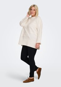 Pull en maille crème claire avec un ourlet côtelé et des rayures texturées, associé à un jean slim noir et des chaussures à lacets marron.