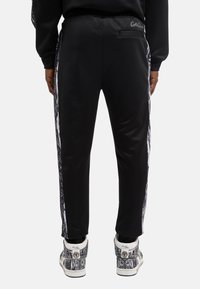 Sorte træningsbukser med slim fit, der har et tekstureret sidelæder, elastisk talje og en baglomme. Matchet med mønstrede sneakers.