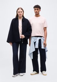 Γυναίκα με μαύρο μπουφάν, ανοιχτό ροζ πουκάμισο, σκούρα τζιν με φαρδιά μπατζάκια, λευκά αθλητικά παπούτσια. Άνδρας με ροζ μπλουζάκι, σκούρο παντελόνι, ριγέ πουκάμισο δεμένο στη μέση, λευκά αθλητικά παπούτσια.