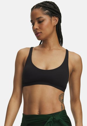 Vrouw met gevlochten haar, gekleed in een zwarte sport-bh en groene broek vastgeknoopt op de taille, toont een gedeeltelijke tatoeage op haar linkerzijde.