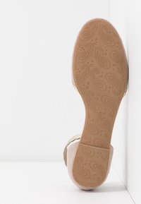 Chaussures avec une semelle en caoutchouc texturée couleur fauve présentant un motif cachemire, une tige en matériau beige doux, et un design subtilement en relief le long des bords.