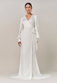 Weißes Wickelkleid mit tiefem V-Ausschnitt, langen Puffärmeln und seitlichem Bindeband. Glattes, fließendes Material mit einem bodenlangen Saum und minimalistischem Design.