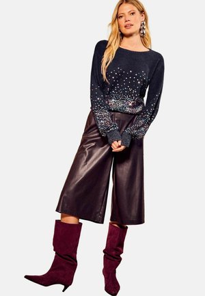 Marineblå sweater med multicolorede detaljer, parret med mørkebrune læder culotter og knæhøje bordeaux ruskindsstøvler.