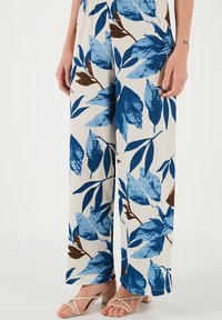 Pantaloni a gamba larga floreali con motivi di foglie blu e marrone su uno sfondo crema. Realizzati in tessuto texturizzato con una vestibilità rilassata.