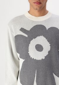 Pullover in Off-White mit einem großen grauen Blumenmuster. Mit einem gerippten Rundhalsausschnitt und weichem, strukturiertem Strickstoff.