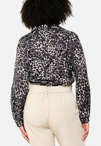 Black and white animal print blouse with long sleeves and a collared neck. Smooth texture; paired with cream-colored elastic waist pants.