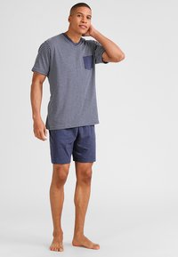 T-shirt a maniche corte, a righe blu e bianche, con taschino sul petto, abbinata a pantaloni corti blu uniformi. Vestibilità casual e tessuto morbido.