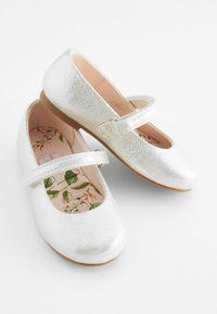 Silberne, metallische Mary Jane Schuhe mit strukturierter Oberfläche, einem Riemen über dem Knöchel und einer blumenmusterierten Innensohle. Flacher Absatz.
