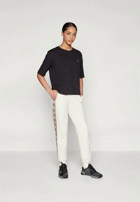 Juodas trumpomis rankovėmis marškinėliai su apvalia iškirpte, derinami su kreminėmis jogger kelnėmis, turinčiomis raštuotą šoninę juostą. Juodi sportiniai batai užbaigia įvaizdį.