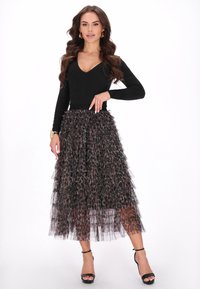 Sort langærmet top med V-udskæring, parret med en leopardmønstret tylnederdel med lagdelte flæser, komplementeret af sorte strophæle.