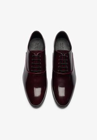 Chaussures habillées en cuir bordeaux avec une finition brillante, ornées de surpiqûres rouges, à bout arrondi et à lacets classiques.