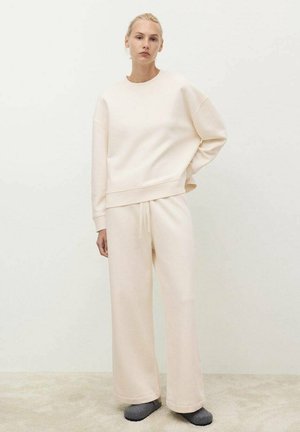Sudadera beige y pantalones de pierna ancha hechos de un material suave. La sudadera tiene un cuello redondo y hombros caídos; los pantalones cuentan con una cintura ajustable mediante cordón.
