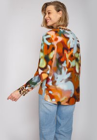 Farbige Seidenbluse mit abstrakten Mustern in Orange, Grün und Blau; Leopardenmuster-Akzente an den Manschetten; lockere Passform; seitliche Schlitze.