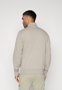 Ανοιχτό γκρι φούτερ με φερμουάρ, διαθέτει ψηλό γιακά και μακριά μανίκια, κατασκευασμένο από απαλό ύφασμα με ριμπ τελειώματα στα μανίκια και το τελείωμα.