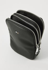 Borsa nera in pelle con tre scomparti con zip, superficie testurizzata, accessori in argento e dettaglio del logo nella parte anteriore.