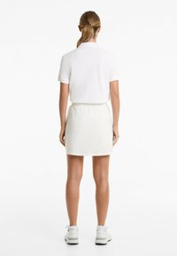 White polo shirt with short sleeves, paired with a light-colored elastic waistband skirt. Casual athletic shoes complete the outfit.