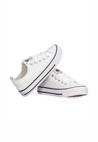 Zapatillas de lona blancas con suelas de goma negras, puntera redonda, diseño con cordones y acentos negros a lo largo de la suela y el logo.