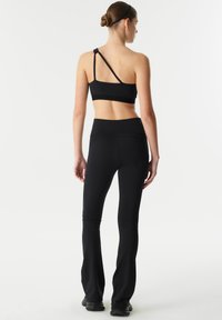 Zwarte sportbeha met verstelbare knoopband, geribbelde textuur; gecombineerd met zwarte uitlopende tights met een hoge tailleband en naadloos ontwerp.