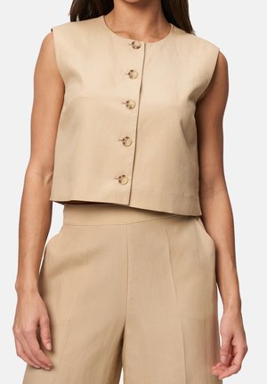 Hihaton beige cropattu toppi, jossa viisi nappia edessä, yhdistettynä vastaaviin korkeavyötäröisiin leveälahkeisiin housuihin mallin päällä.
