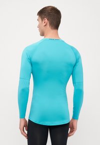 Lyseblå langærmet træningsskjorte med en tætsiddende pasform, glat tekstur og Nike Pro-logo på den øverste del af ryggen.