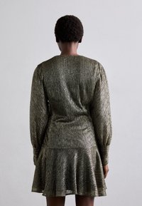 Robe en bronze métallique avec des manches longues et une jupe évasée, présentant une surface texturée et un motif côtelé sur le tissu.