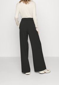 Black wide-leg trousers with an elastic waistband, featuring a smooth texture and a loose fit. Paired with light-colored long-sleeve top.