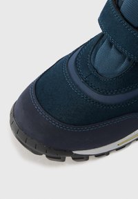Scarpa in suede blu navy e tessuto con cinturino in velcro, punta arrotondata, suola in gomma testurizzata e cuciture azzurre in contrasto.