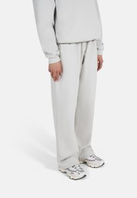 Lysegrå oversized sweatshirt og matchende vide bukser i mykt stoff. Kombinert med grå og hvite chunky sneakers. Hender synlige med ringer.