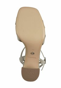 Sandal beige con suola in gomma testurizzata, dettagli metallici e design a tracolla curva. Presenta una cinturino alla caviglia regolabile e tacco piatto.