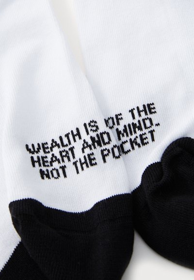 White cotton socks featuring black text that reads "WEALTH IS OF THE HEART AND MIND, NOT THE POCKET." Black accent at the toe.
