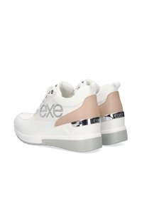 Zapatillas blancas con suela de goma gris, con un acento metálico y un panel de talón de cuero beige. Adornadas con un logo plateado.