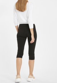 Černé capri kalhoty s přiléhavým střihem, zdobené řasením na lemu a zadních kapsách. Kombinovány s bílým dlouhým rukávem.
