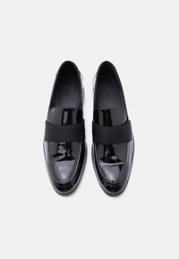 Γυαλιστερά μαύρα loafers χωρίς κορδόνια με πλατιές ελαστικές λωρίδες πάνω από το πέλμα, σε θέαση από πάνω σε λευκό φόντο.