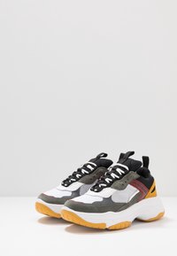 Baskets chunky présentant un mélange de matériaux blancs, noirs, gris et oranges. Les textures en maille, en daim et en caoutchouc mettent en valeur le design.