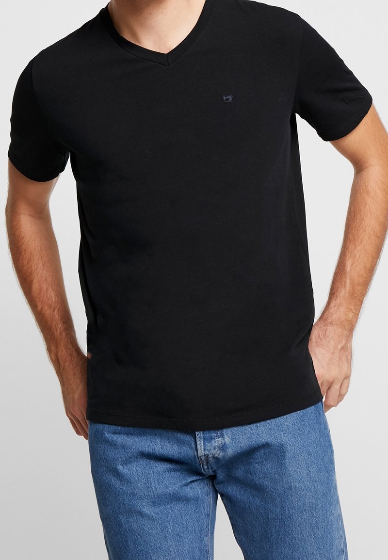 Sort kortærmet V-hals t-shirt lavet af blødt bomuldsstof. Har et lille logo på brystet. Kombineret med blå denim jeans.