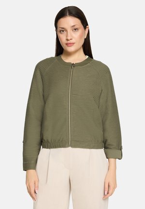 Olivengrøn lynlåstrøje med tekstureret ribbet materiale, kort design og elastisk taljebånd; har manchetter på ærmerne og rund halsudskæring.