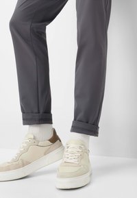 Grijze, taps toelopende broek met opgerolde boorden, gecombineerd met lichtbeige sneakers met suède- en leren accenten. Witte sokken zichtbaar.