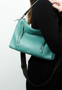 Teal leren schoudertas met een gebogen ontwerp, voorzien van twee ritszakken, een afneembare bruine schouderband en een subtiele logo-accent.