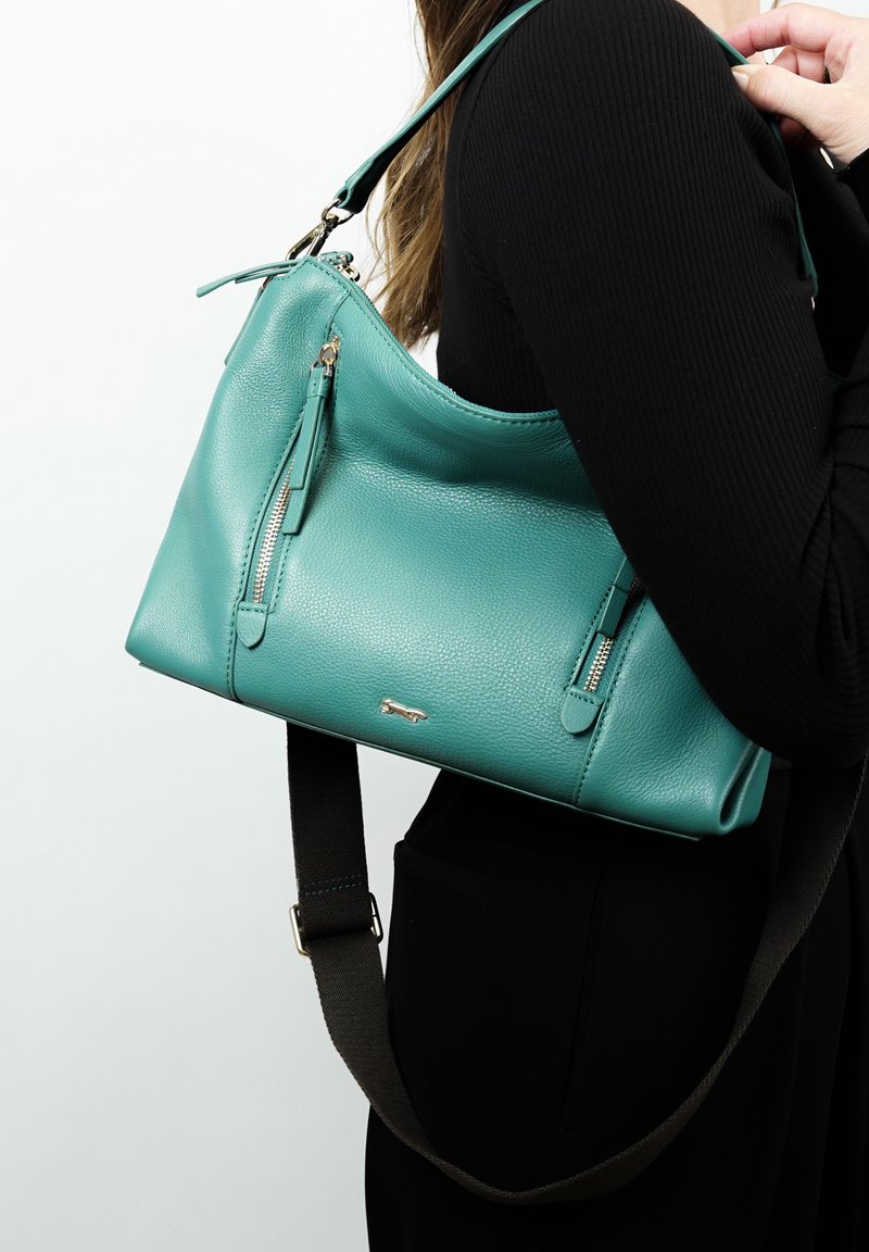 Teal leren schoudertas met een gebogen ontwerp, voorzien van twee ritszakken, een afneembare bruine schouderband en een subtiele logo-accent.