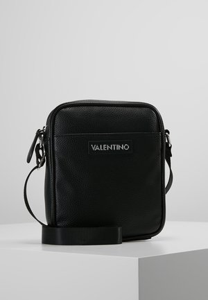 Black leather crossbody bag with a textured surface, rectangular shape, zip closure, and a prominent logo plaque on the front.