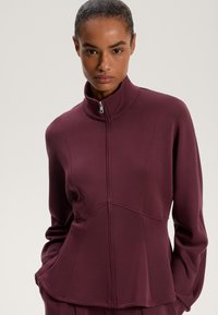 Bordó zip-up bunda s vysokým límcem, strukturovanou tkaninou a přizpůsobenými švy. Obsahuje peplum design a přední kapsy.