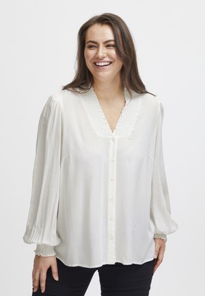 Vit blus med V-ringning och texturerade detaljer, med långa, ballongärmar och draperade manschetter. Slät tyg med subtila ränder.