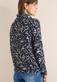 Haut à manches longues bleu marine et crème avec un motif de feuilles, une texture douce et un col à revers, porté avec un jean en denim.
