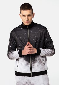 Chaqueta negra y blanca con cremallera que presenta un patrón de galaxia, con un alto cuello, puños acanalados y una textura suave.