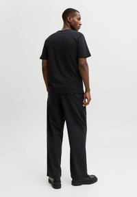 Juodas medvilnės marškinėliai trumpomis rankovėmis, apvaliu iškirpimu ir laisvu siluetu, derinami su juodomis kelnėmis, turinčiomis laisvą dizainą ir minimaliais akcentais.