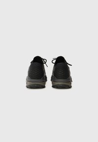 Zapatillas deportivas negras con parte superior de tejido texturizado, cordones planos y suela de goma gris. Diseño minimalista sin logotipos visibles.