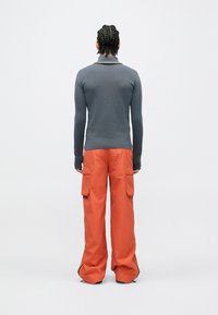 Camisola cinzenta de manga comprida, corte justo, combinada com calças cargo laranja brilhante, com bolsos laterais e corte largo, detalhes mínimos.